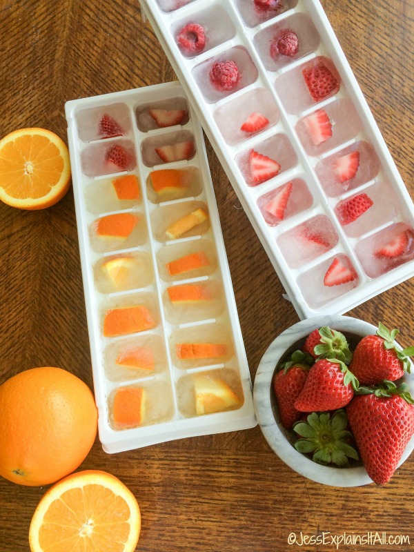 Two trays of fruit infused ice cubes next to strawberries and oranges.