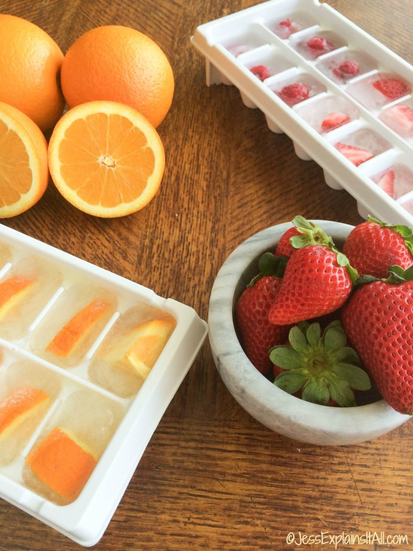 Orange ice cubes, strawberry ice cubes and raspberry ice cubes next to fresh fruit.