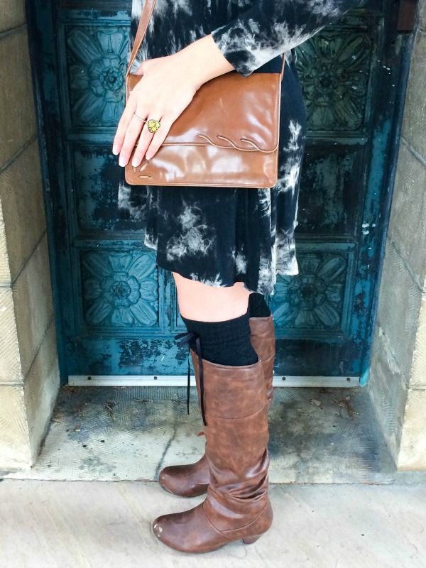 A girl in a black dress with a brown purse and brown boots.