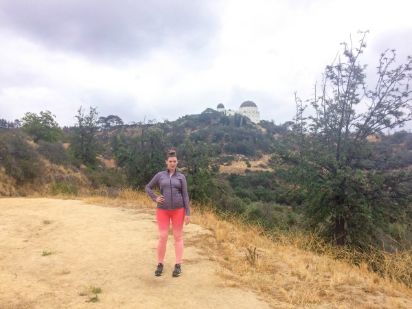 A girl standing on a hiking trail in front of the Griffith Observatory.