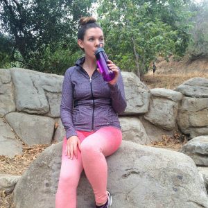Girl drinking water sitting on a stone.