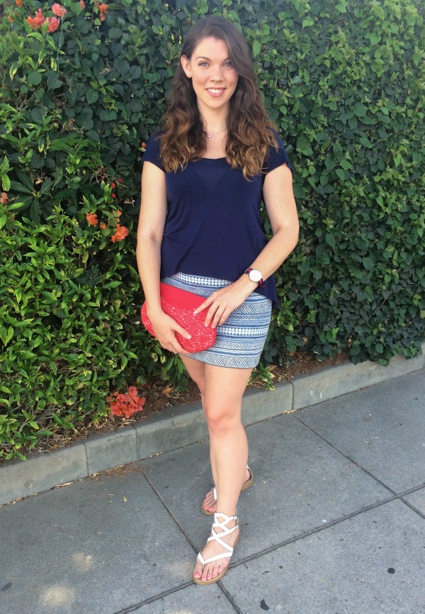 Brunette standing in front of a green hedge wearing a red, white and blue outfit.