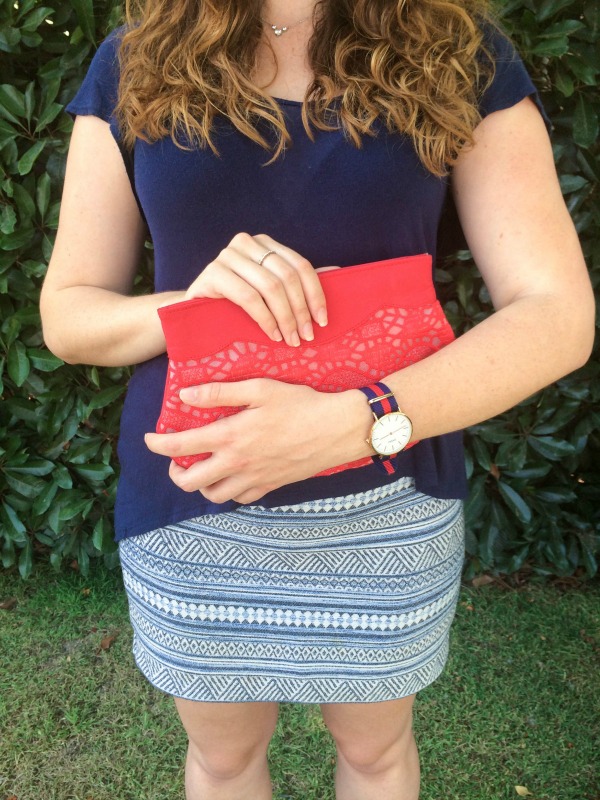 A girl holding a red clutch wearing a blue patterned skirt.