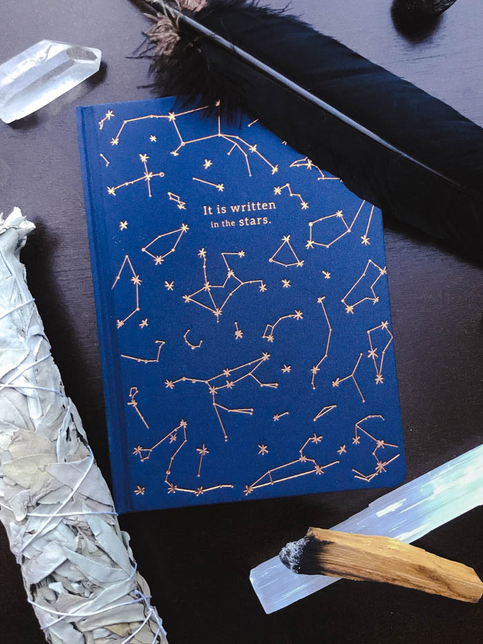 An assortment of smudging items arranged around a notebook with constellations on it.
