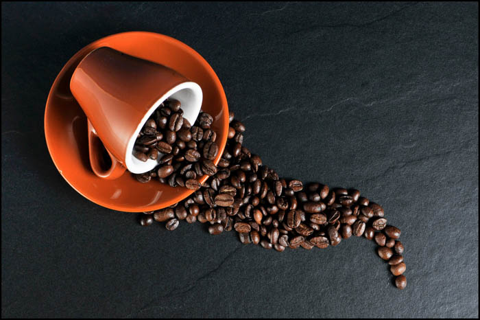 coffee beans flowing out of an orange coffee cup and saucer. An orange coffee cup with coffee beans in it.